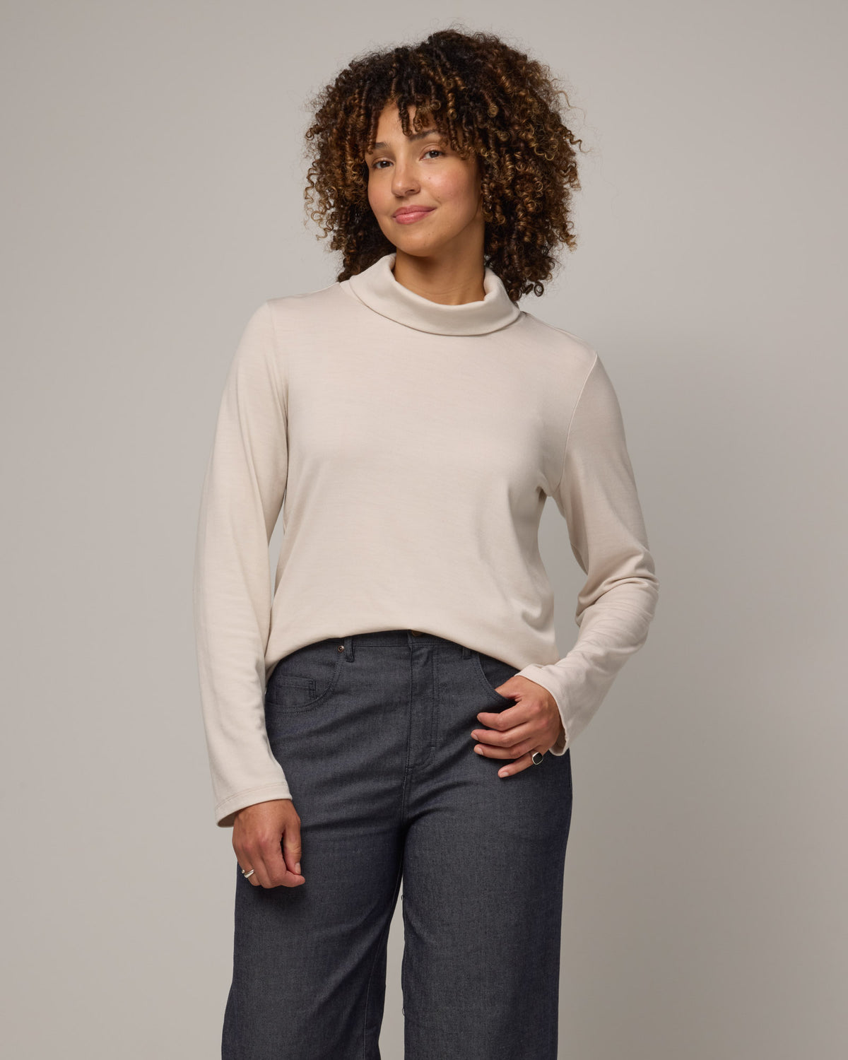 Model wearing Rylie Heavyweight Turtleneck Top in Oatmeal, a light cream color. Rylie Heavyweight Turtleneck Top is a merino wool long sleeve, relaxed fit turtleneck available in sizes XS-3X.