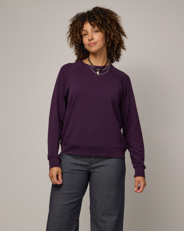 Model wearing Aspen Sweatshirt in Cassis, a dark purple color. Aspen Sweatshirt is a merino wool long sleeve, crew neck, regular fit sweatshirt available in sizes XS-3X.