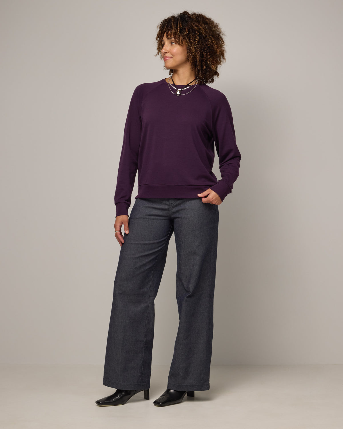 Model wearing Aspen Sweatshirt in Cassis, a dark purple color. Aspen Sweatshirt is a merino wool long sleeve, crew neck, regular fit sweatshirt available in sizes XS-3X.