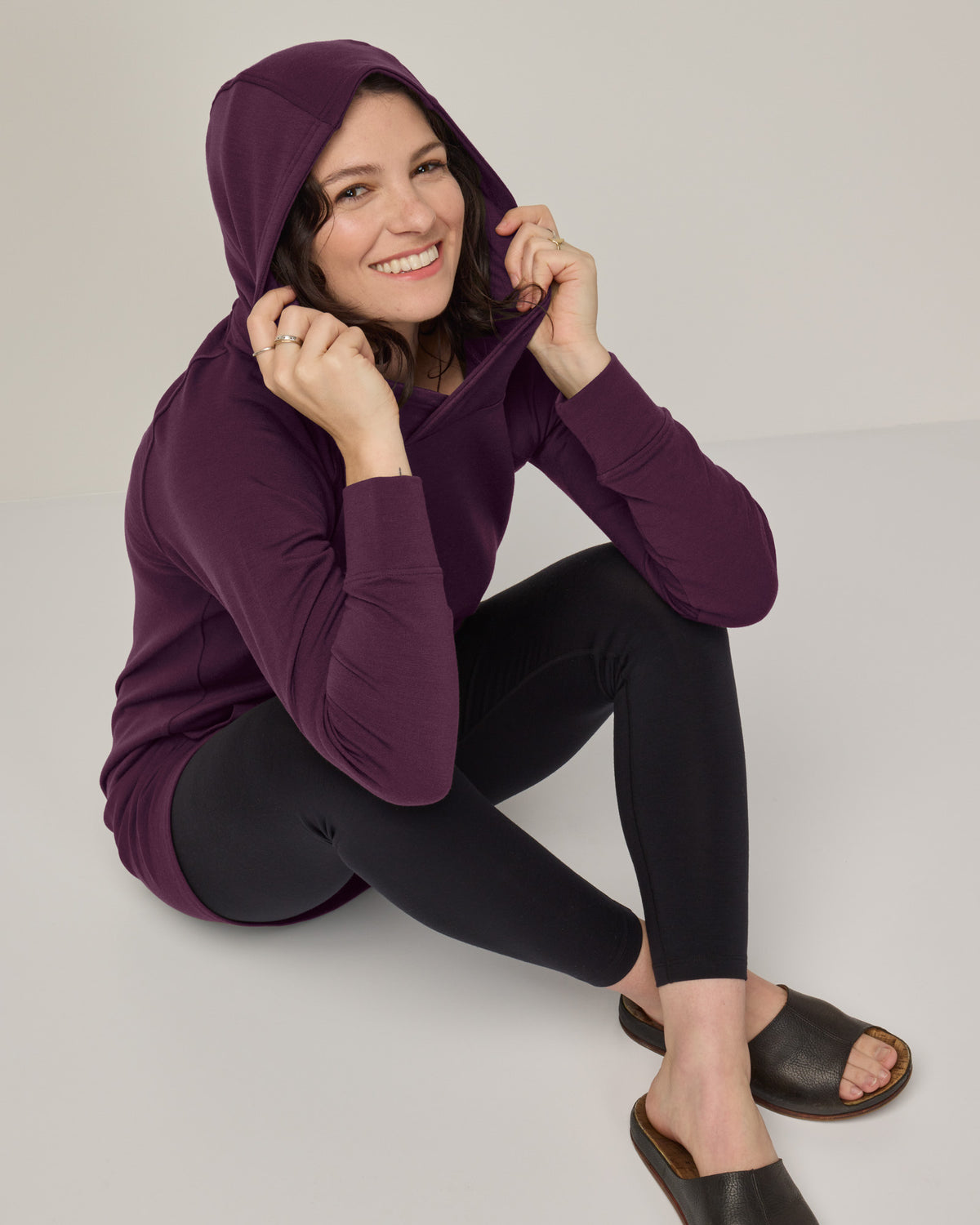 Model wearing Everett Hoodie Tunic in Marionberry, a dark berry purple color. Everett Hoodie Tunic is a merino wool long sleeve, crew neck, Tunic fitted sweatshirt with pockets available in sizes XS-3X.
